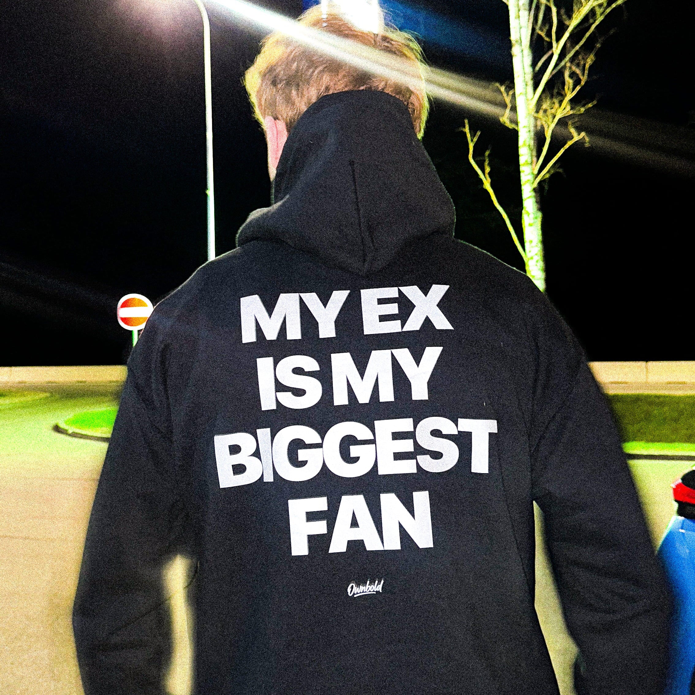 Person wearing a black hoodie with text on the back at night.