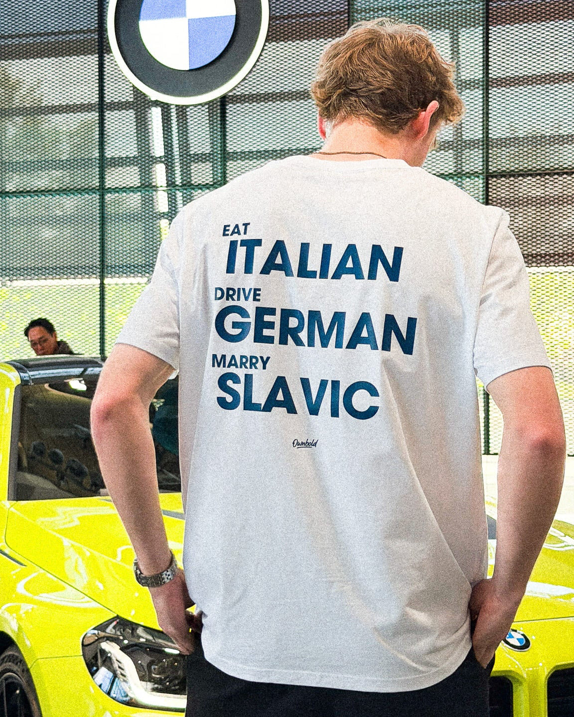 Person wearing a t-shirt with text in front of a BMW vehicle